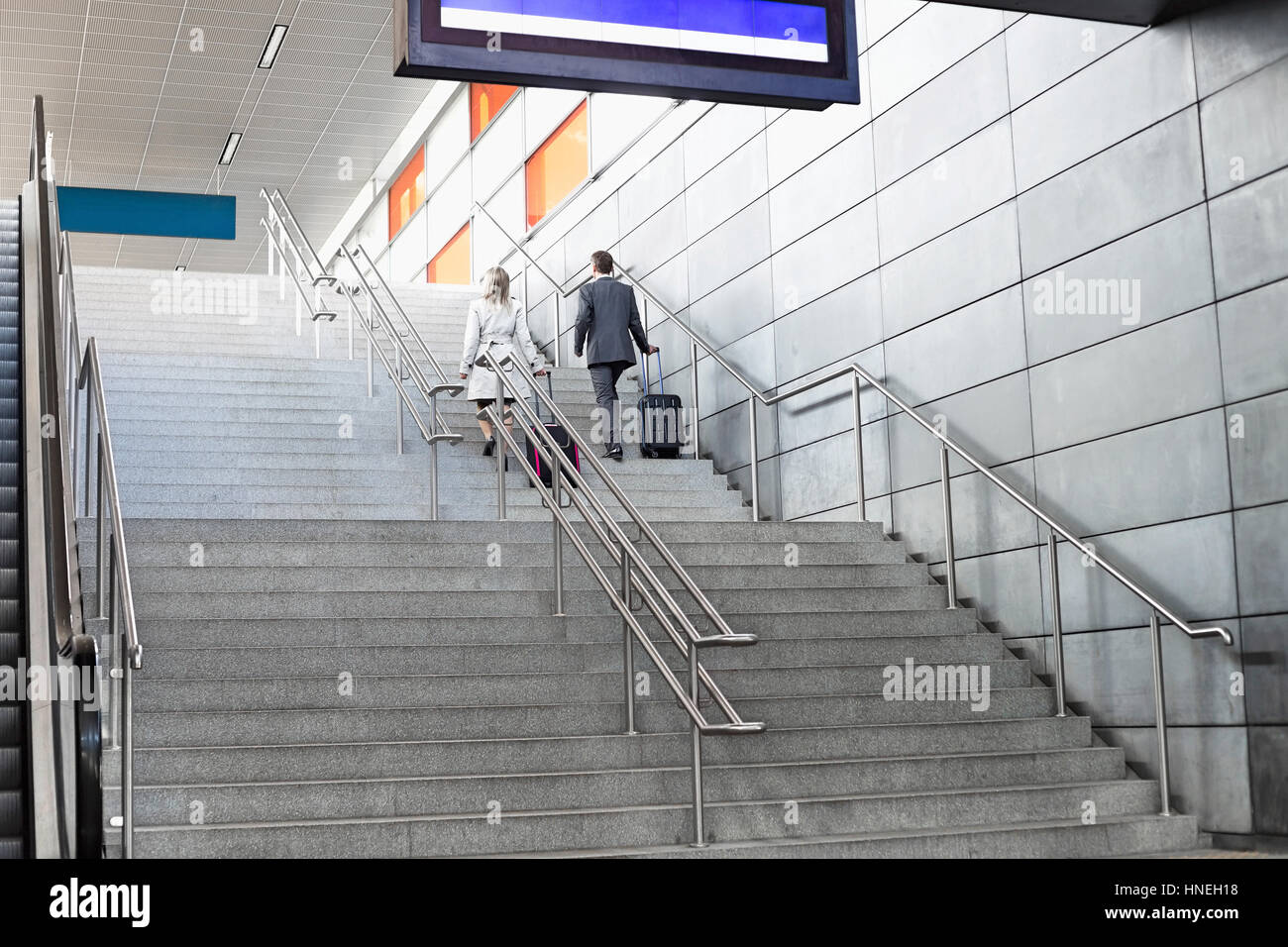 Rear view of businesspeople with luggage moving upstairs in railroad station Stock Photo