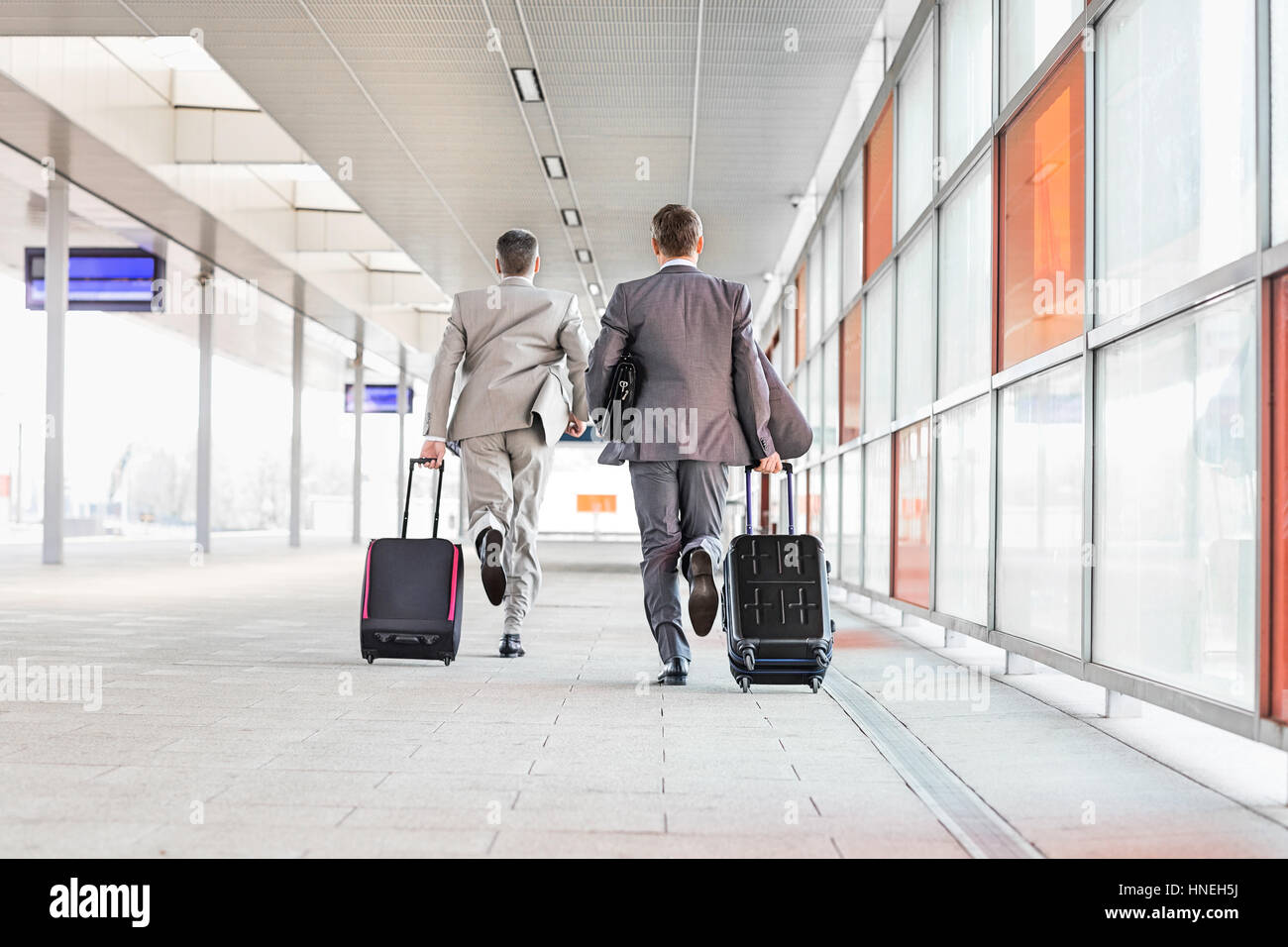 Full length rear view of businessmen with luggage running on railroad platform Stock Photo