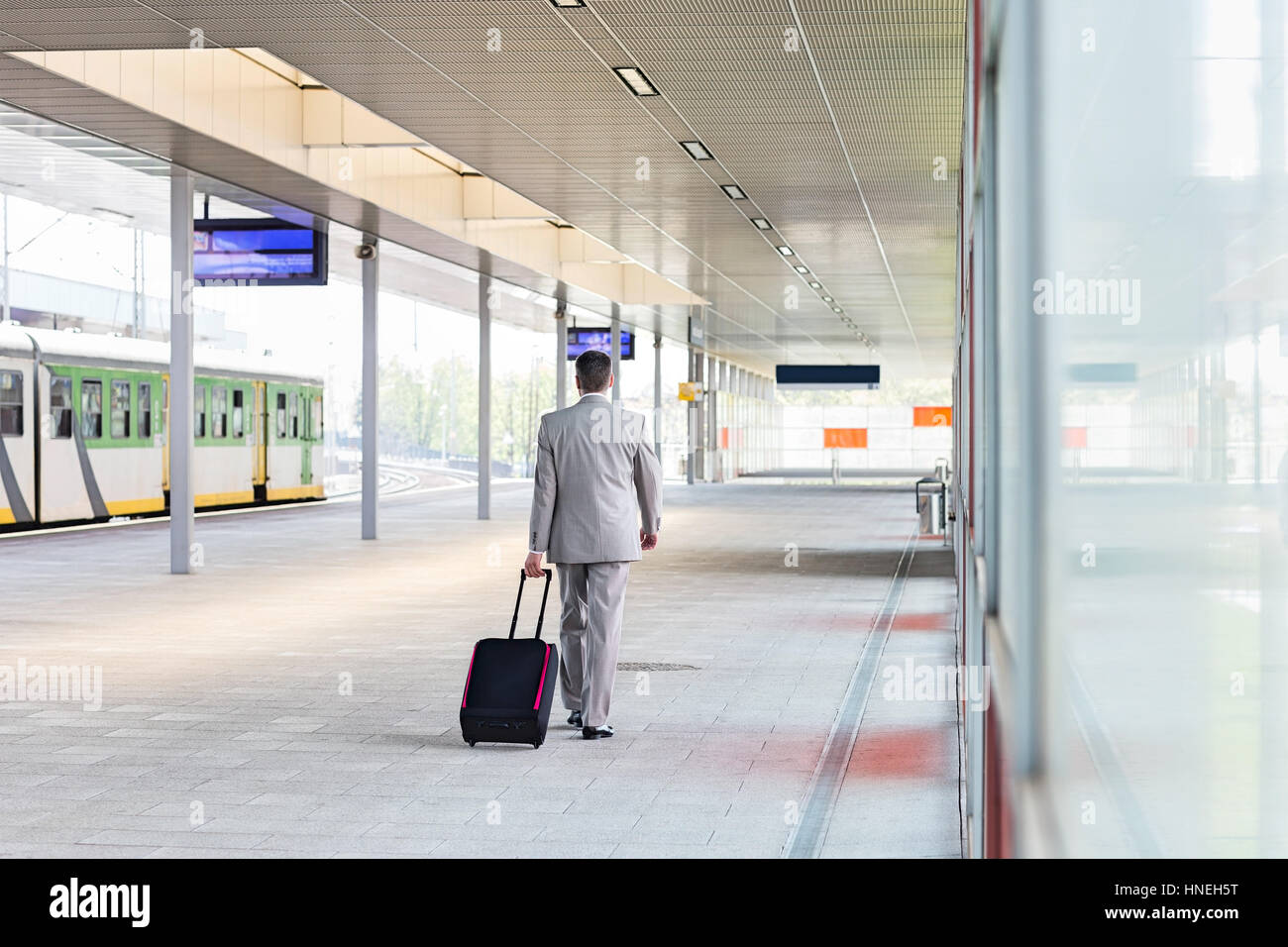 Full length rear view of businessman with luggage walking in railroad platform Stock Photo