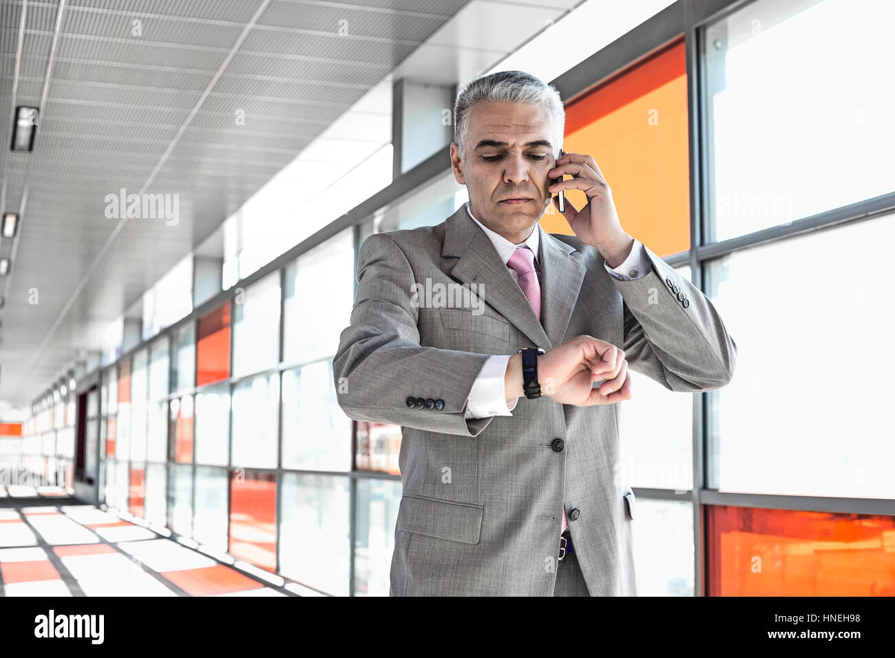 Middle aged businessman checking time while on call at railroad station ...