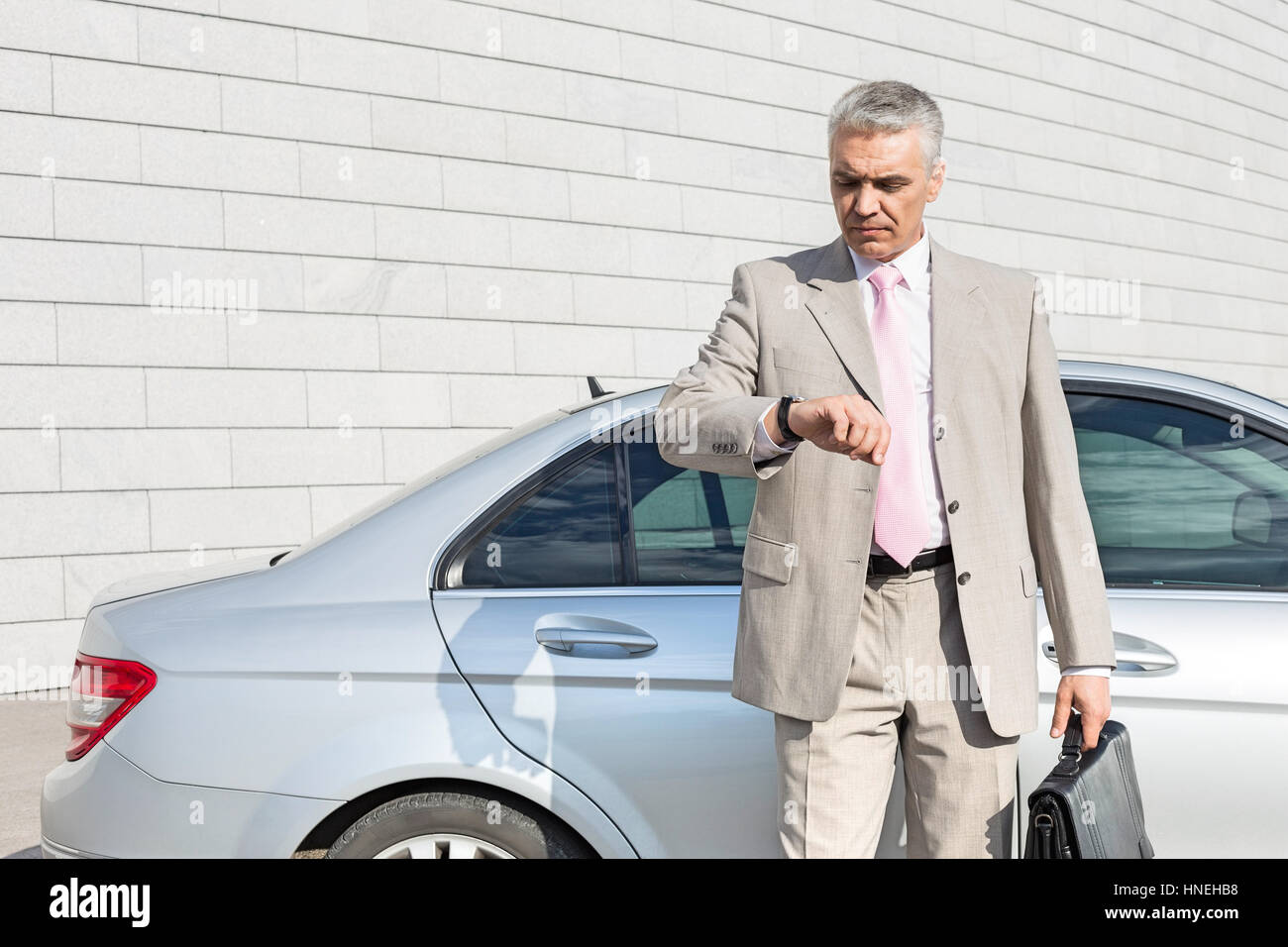 Businessman checking the time in front of car outdoors Stock Photo
