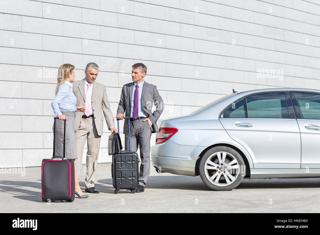 Businesspeople with luggage discussing outside car on street Stock Photo