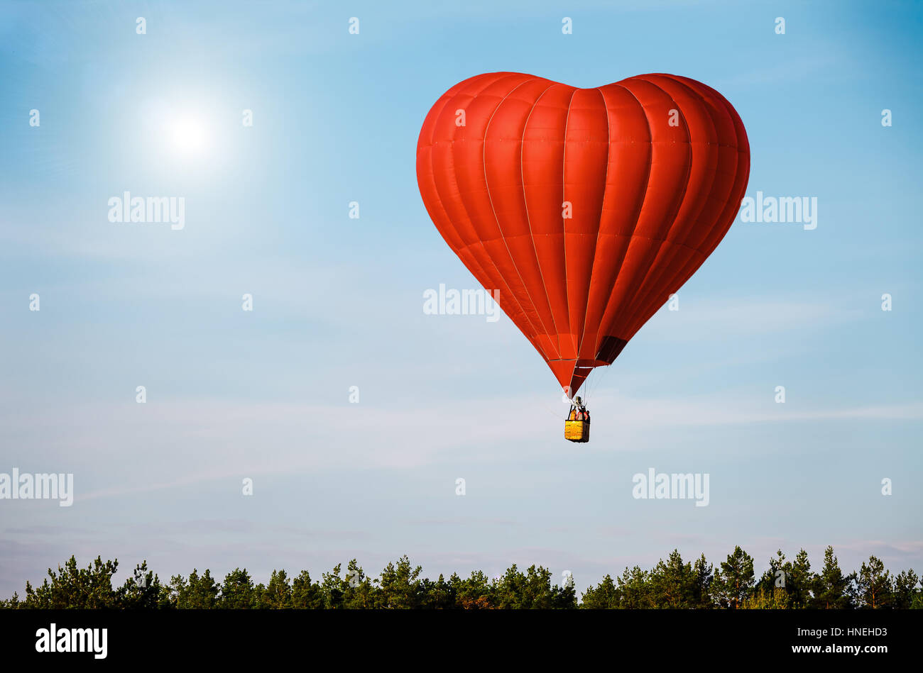 Red air balloon in the shape of a heart flying in blue sky Stock Photo