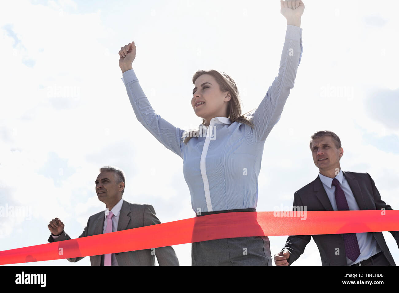 Low angle view of businesswoman crossing finishing line with colleagues in background Stock Photo