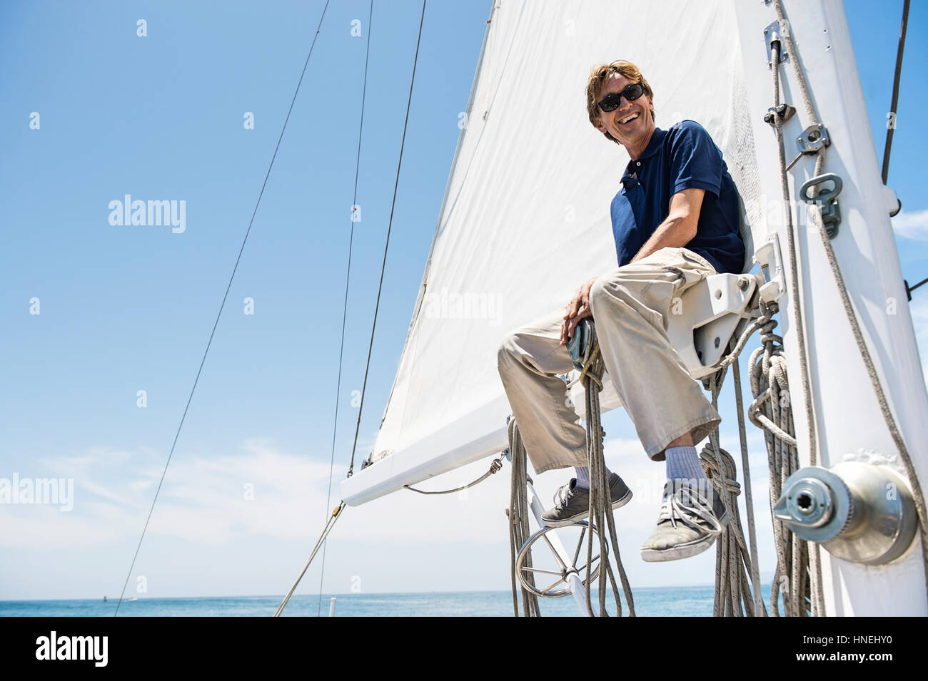 Low angle view of smiling man sitting on yacht boom Stock Photo