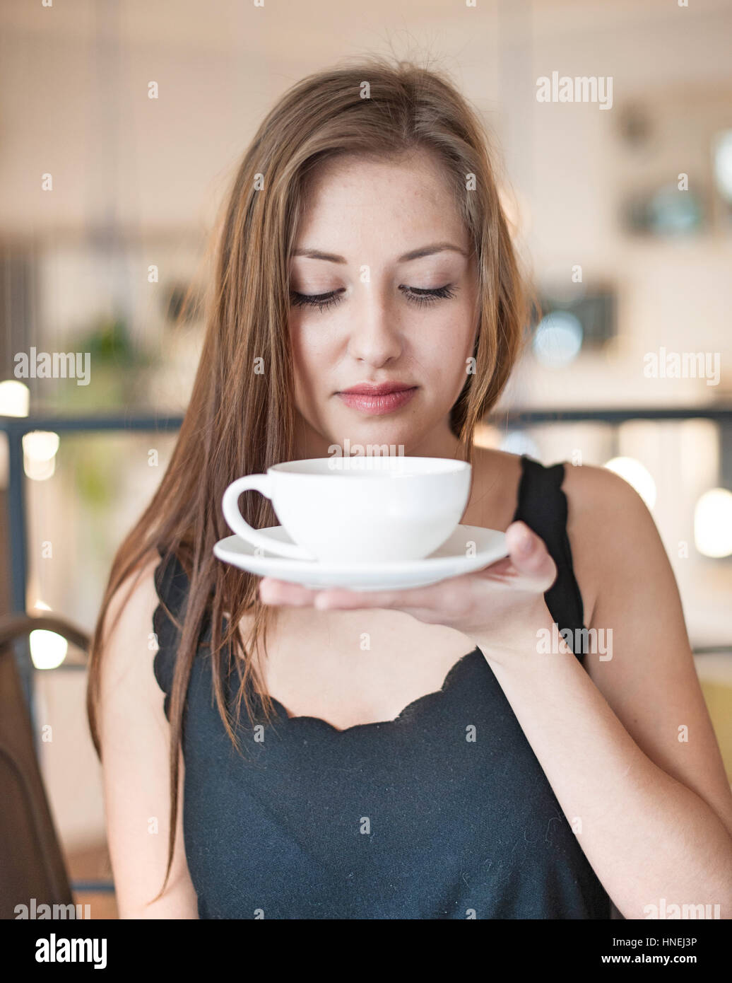Beautiful young woman holding coffee cup and saucer at cafe Stock Photo