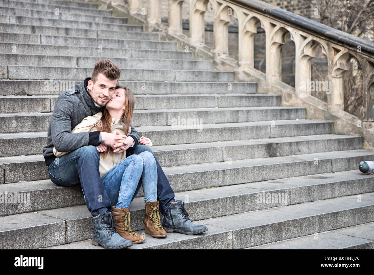 Full length of loving woman kissing man while sitting on steps outdoors Stock Photo