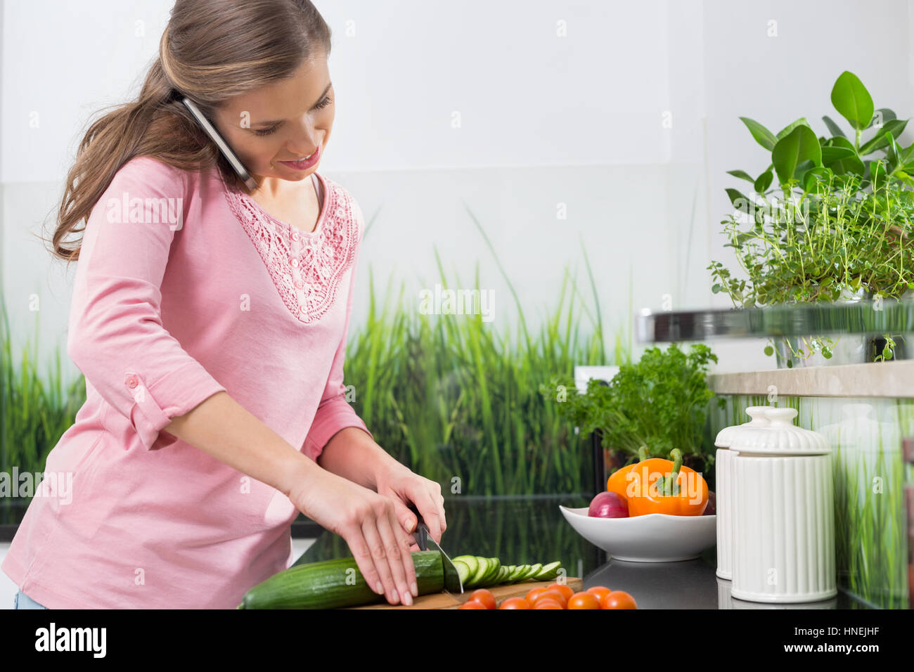 Woman using cell phone while cutting cucumber at kitchen counter Stock ...