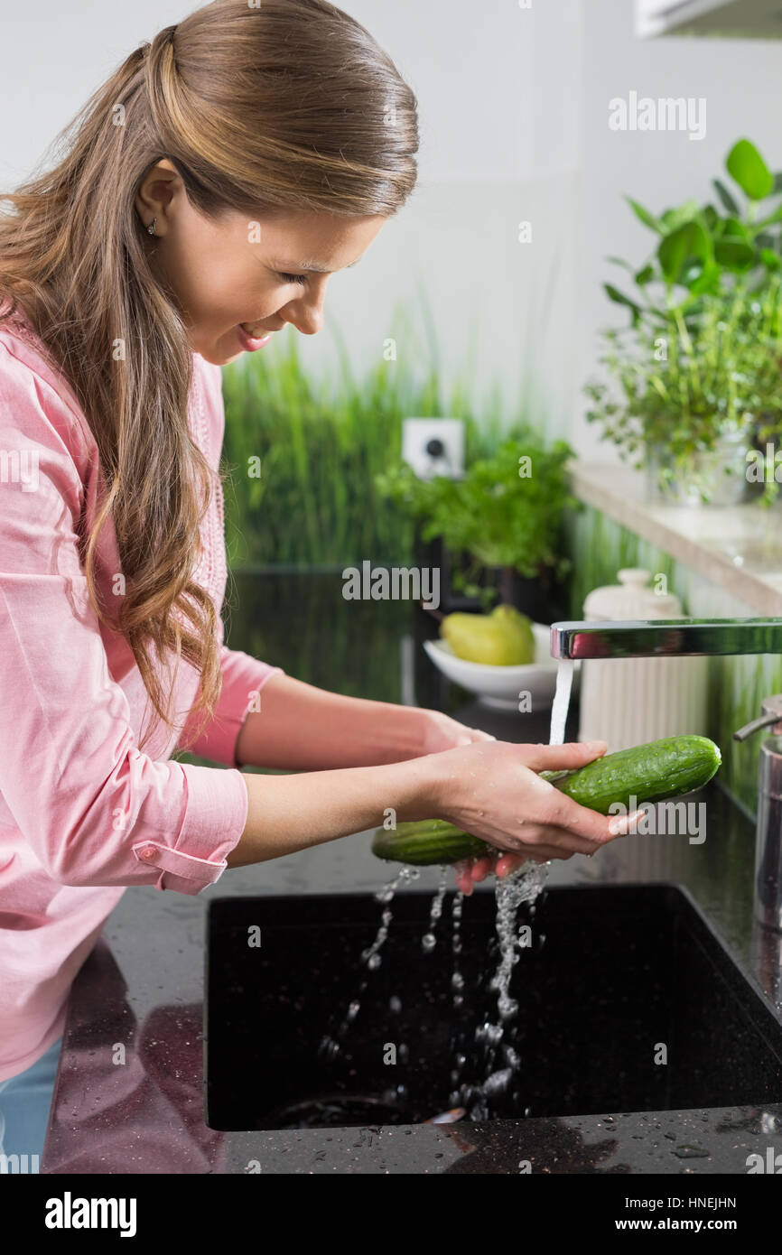 Smiling woman washing cucumber in kitchen Stock Photo