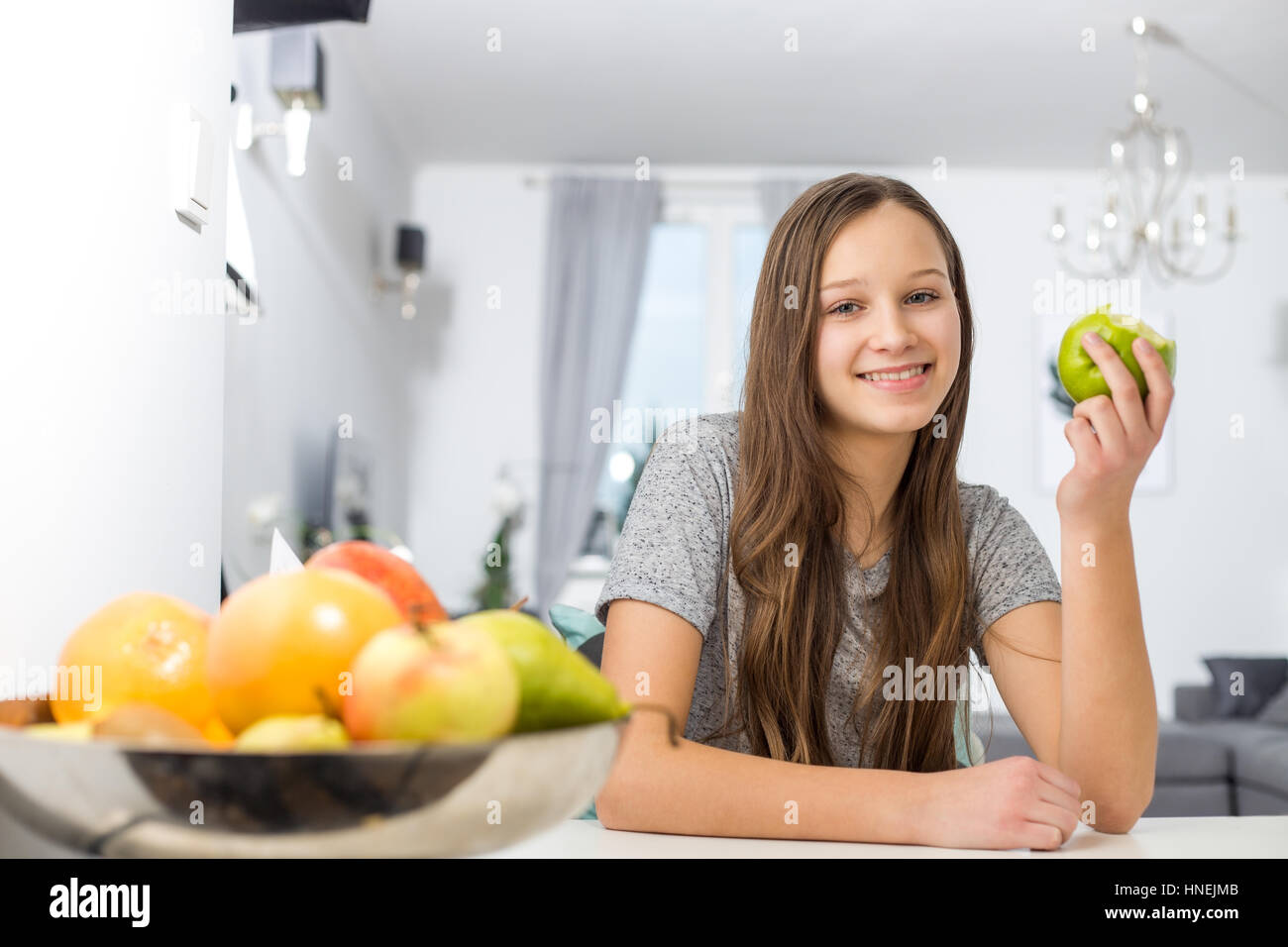 Portrait of smiling girl holding apple while sitting at table in house Stock Photo