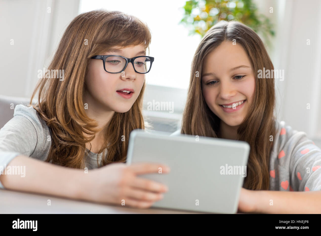 Sisters using digital tablet at table in house Stock Photo - Alamy