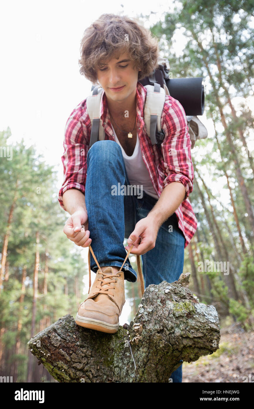 Full length of male backpacker tying shoelace in forest Stock Photo