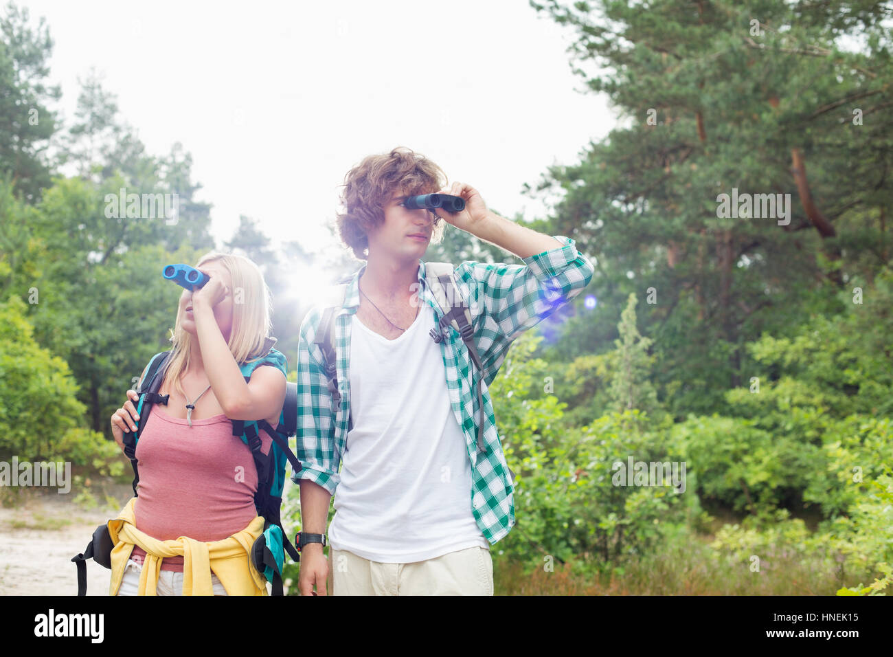 Young couple using binoculars while hiking in forest Stock Photo