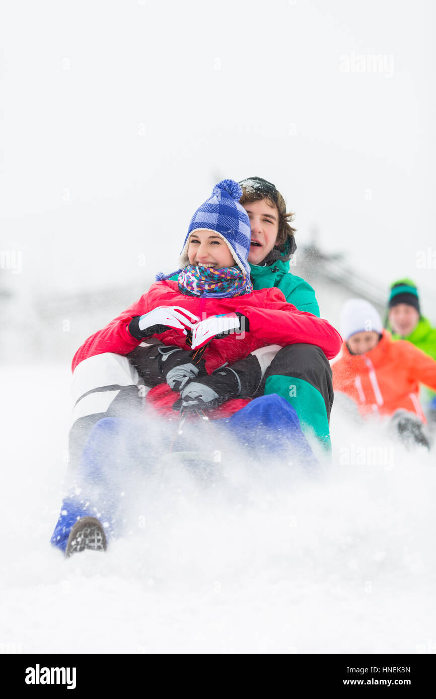 Excited young friends sledding in snow Stock Photo