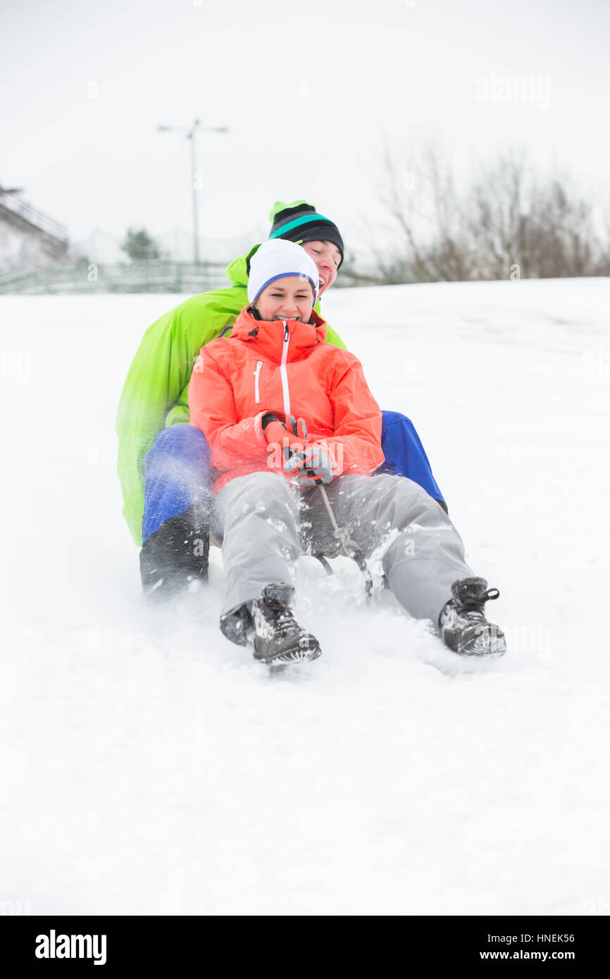 Full length of young couple sledging on snow covered land Stock Photo