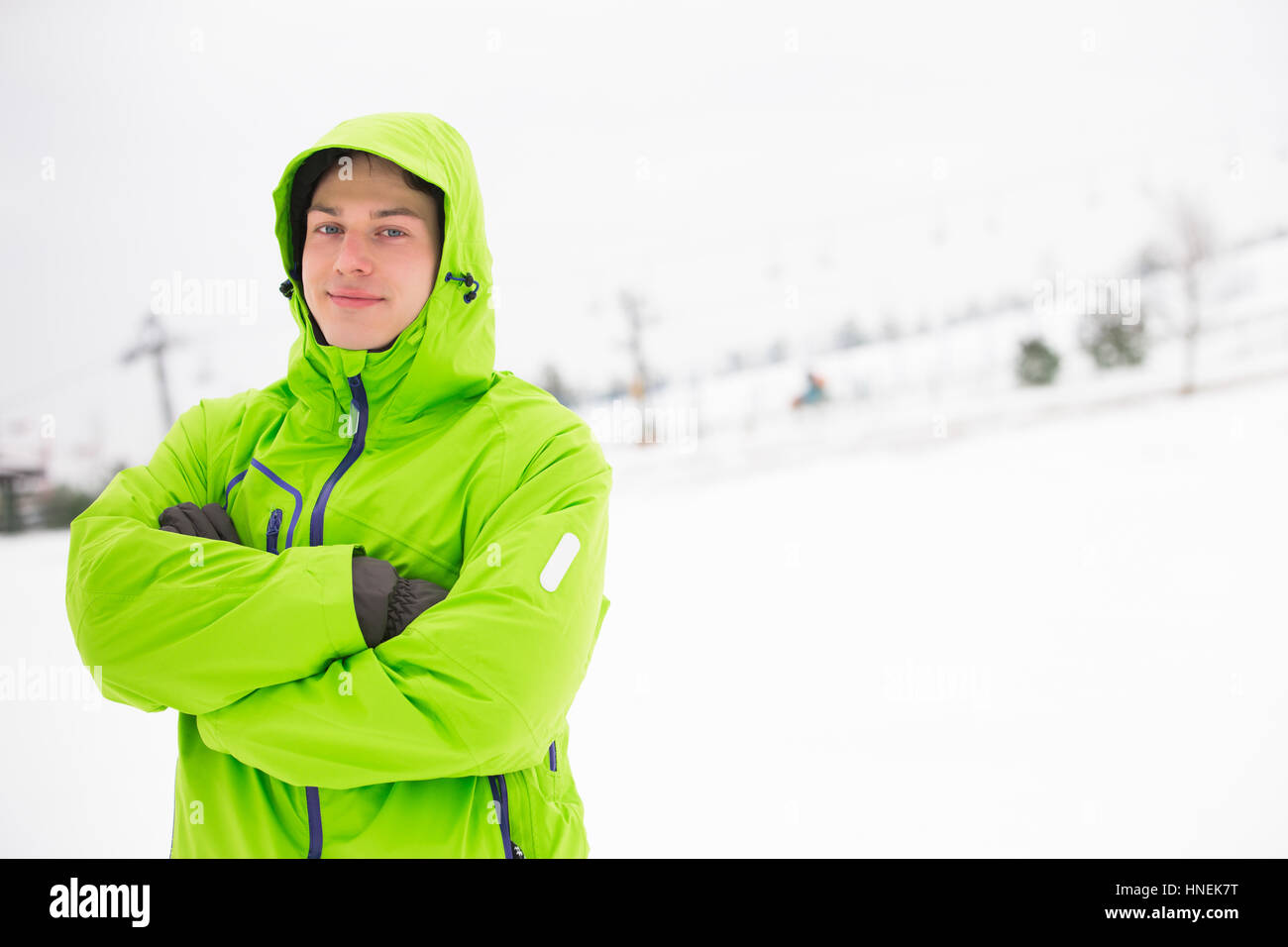 Portrait of young man in hooded jacket standing arms crossed in snow Stock Photo