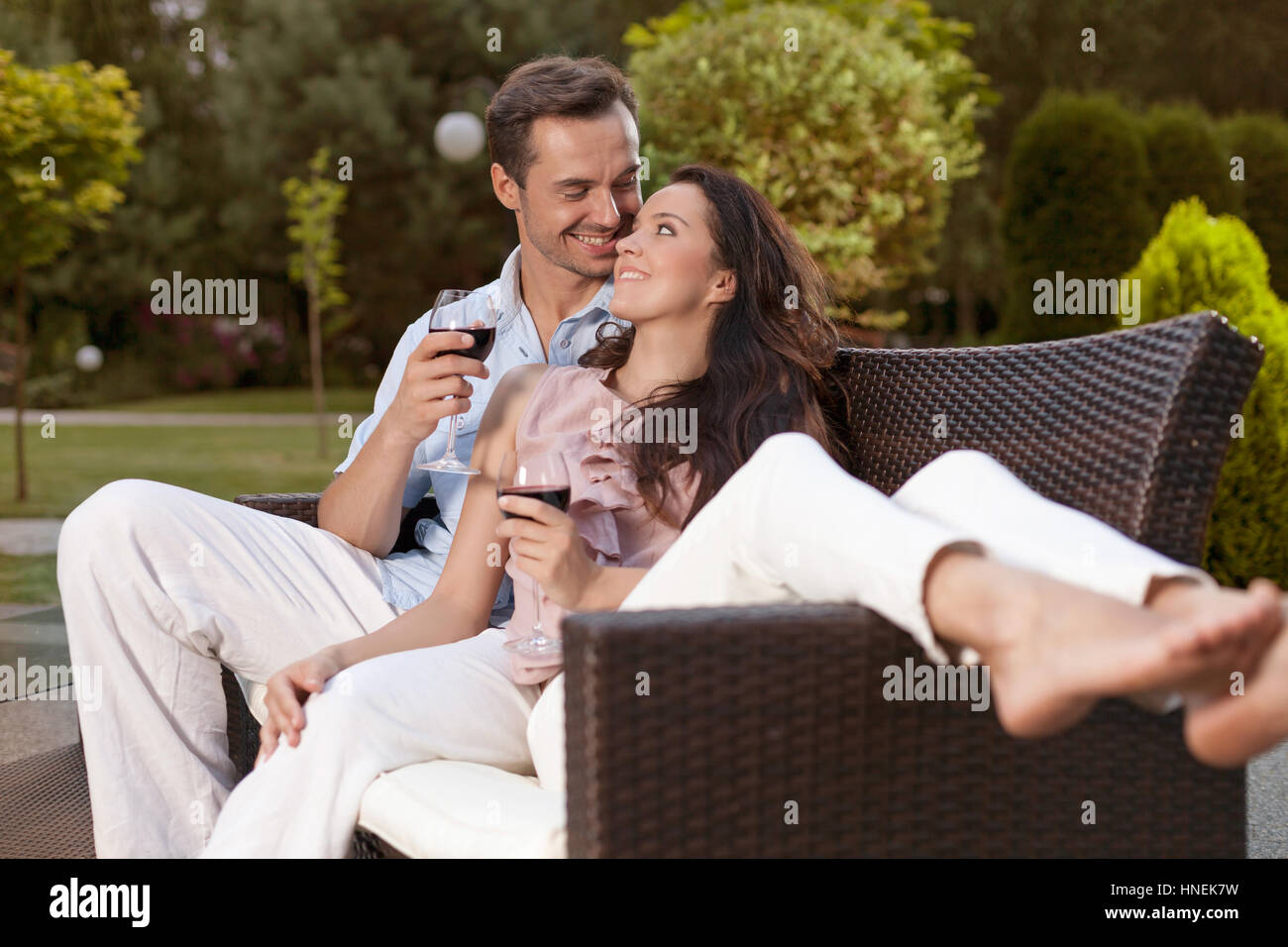 Romantic young holding wine glasses on easy chair in park Stock Photo