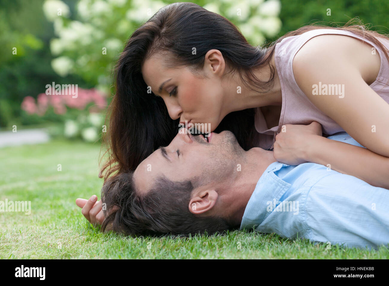 Side view of young woman kissing man while lying in park Stock Photo ...