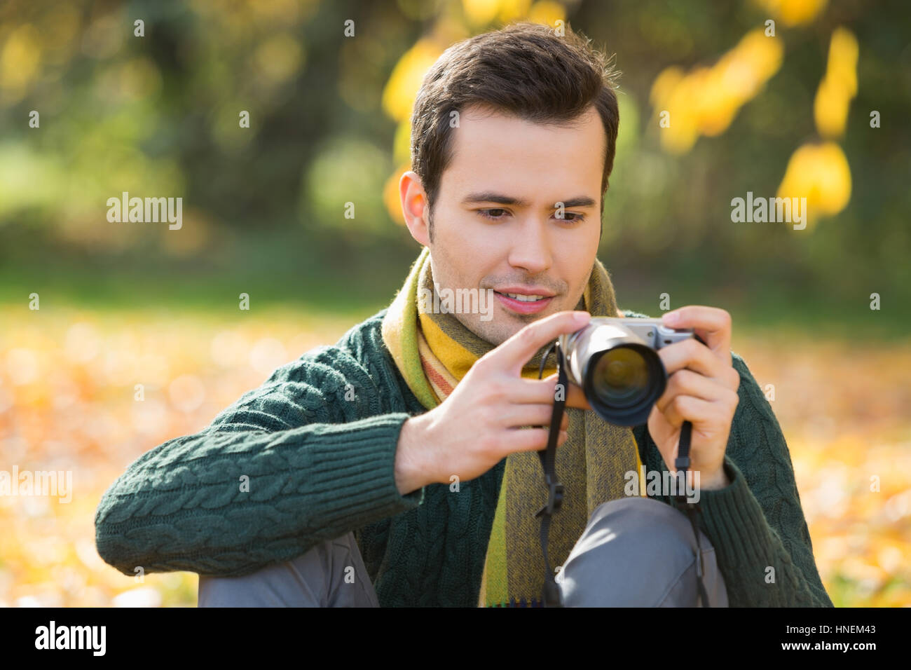 Young man watching photographs on digital camera in park during autumn Stock Photo