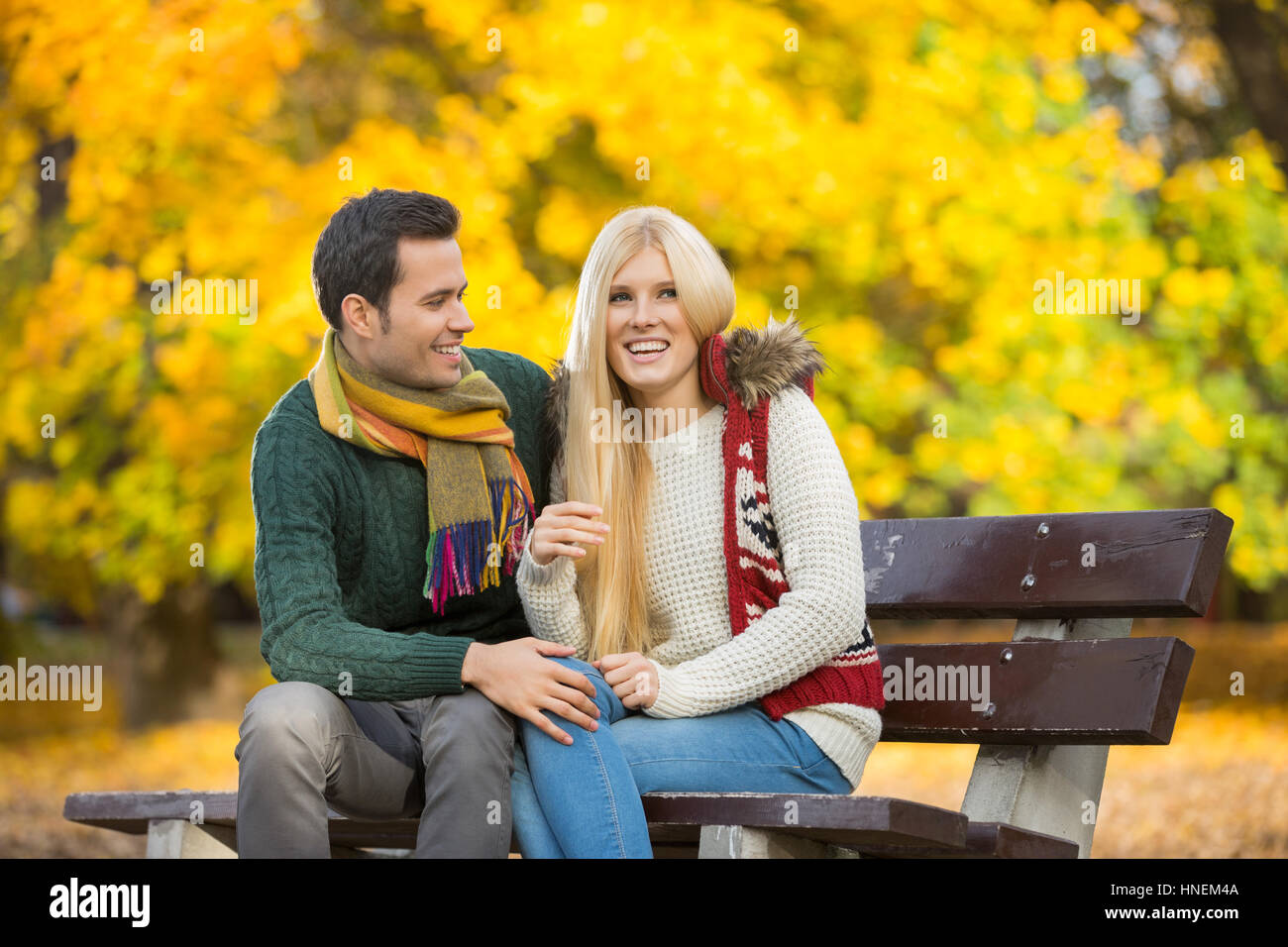 Happy young couple sitting on park bench during autumn Stock Photo - Alamy