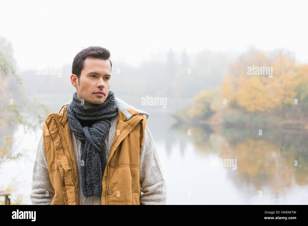 Thoughtful young man in warm clothing standing against lake Stock Photo