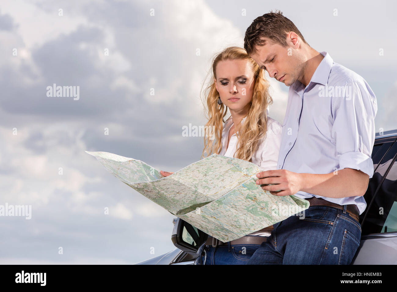 Couple reading map while leaning on car against cloudy sky Stock Photo