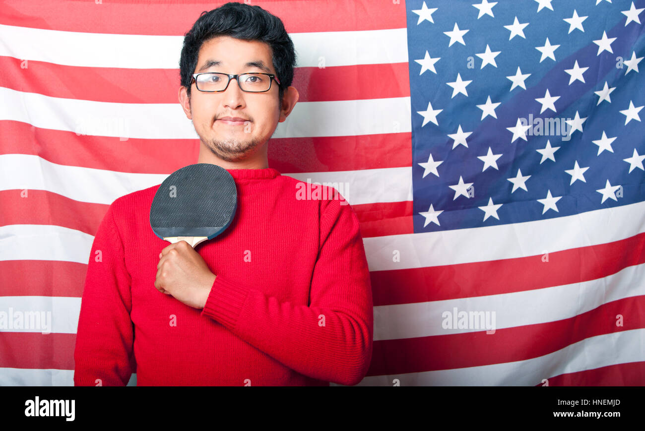 Proud Asian Man holding table tennis paddle against US Flag Stock Photo