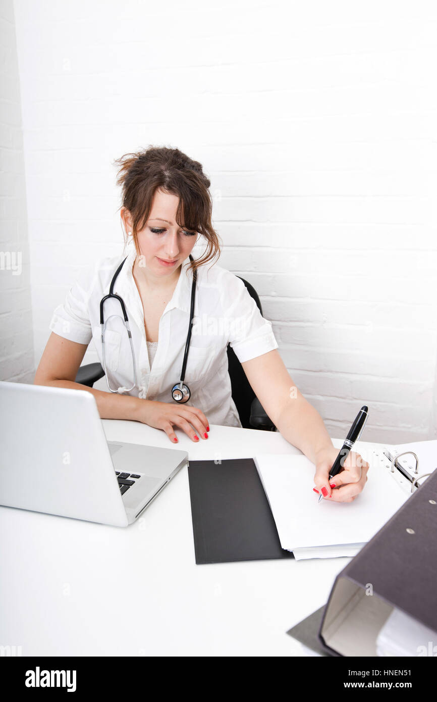 Young female doctor writing notes on desk in clinic Stock Photo