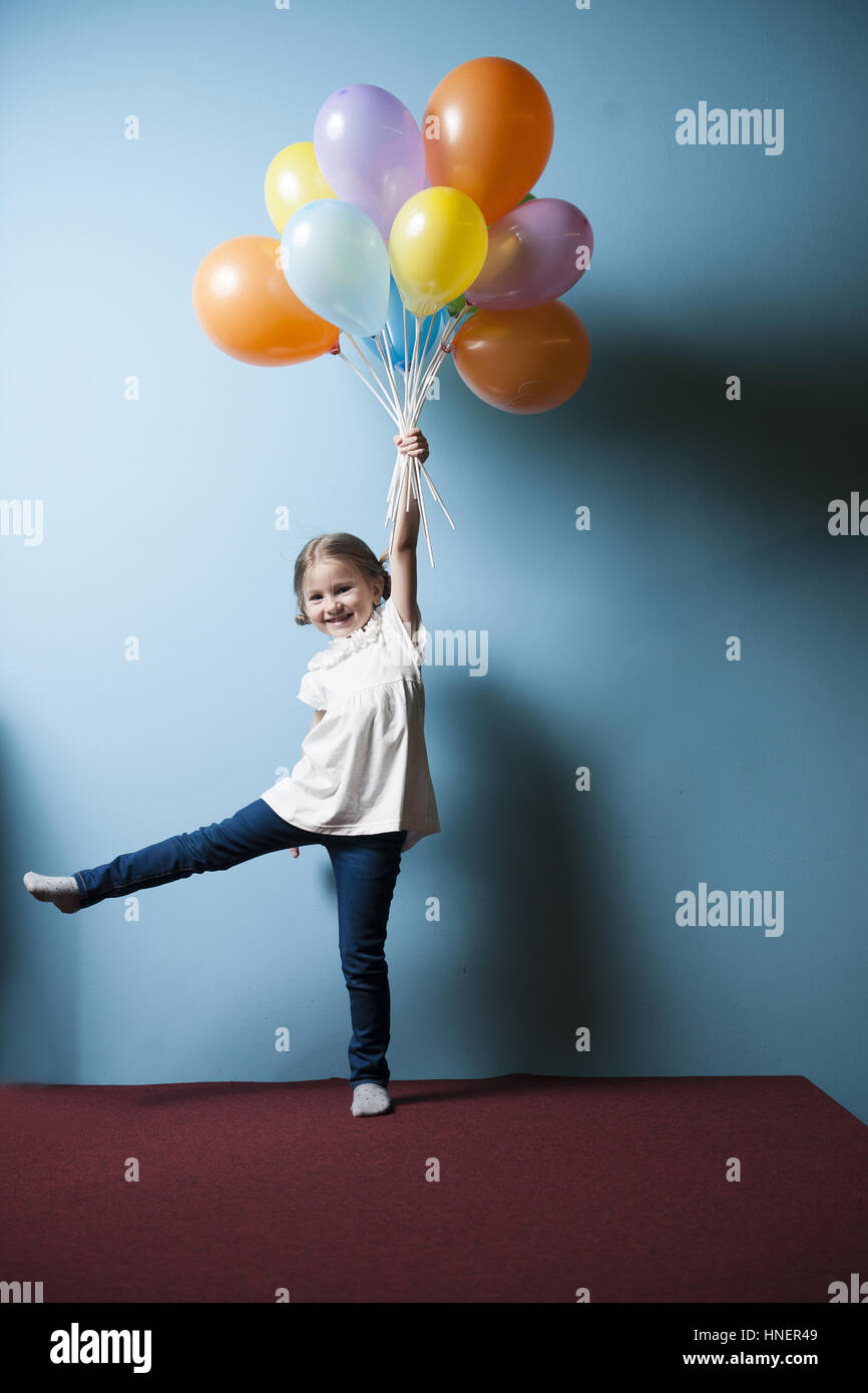 Young girl pretending to be lifted up by bunch of balloons Stock Photo