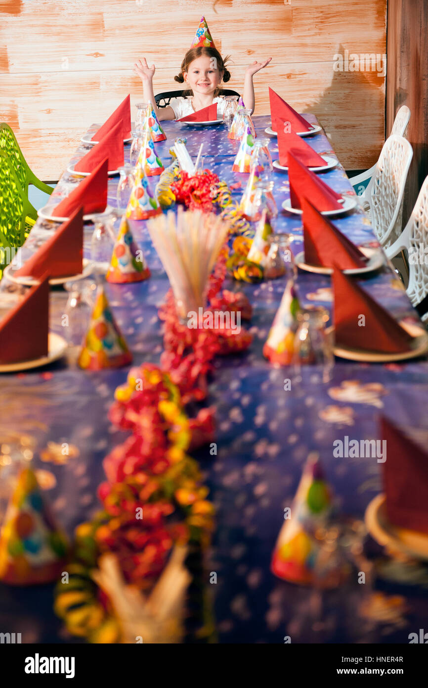 Happy young girl at her dinner party table wearing party hat Stock