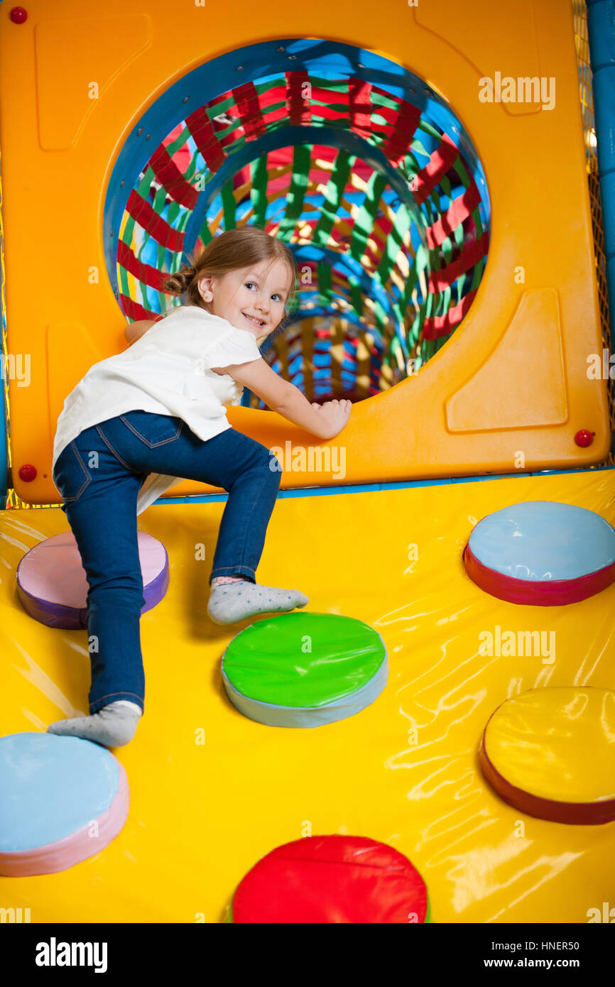 Young girl climbing up ramp into tunnel at soft play centre Stock Photo