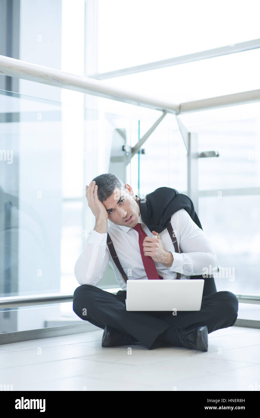 Stressed out businessman seated on floor working at laptop Stock Photo
