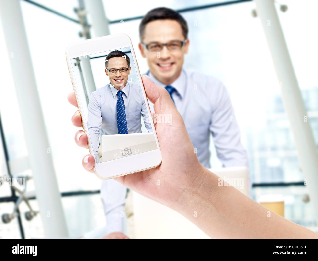 hand of a female holding a cellphone taking a picture of a smiling business man in office. Stock Photo