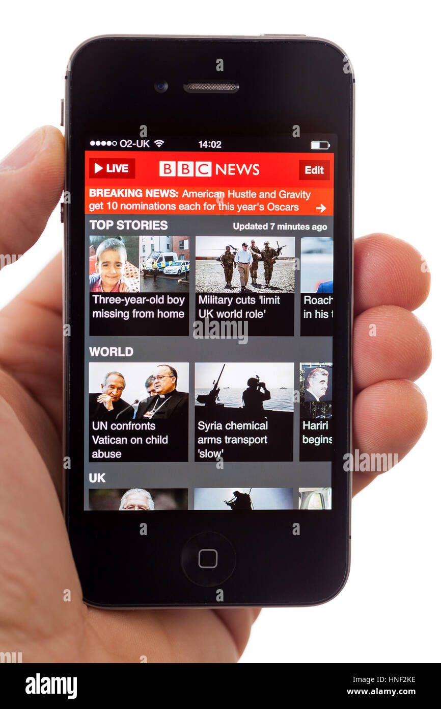BATH, UK - JANUARY 16, 2014: A hand holding an Apple iPhone 4s displaying the front page of the BBC News App, against a white background. The app can  Stock Photo