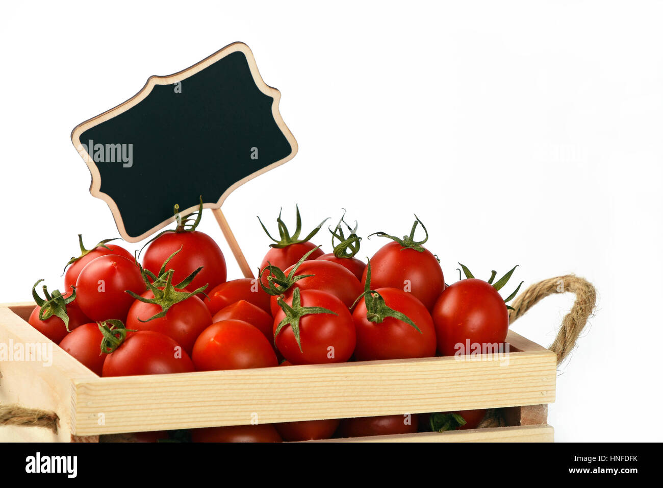Fresh red ripe cherry tomatoes in small wooden box with black chalkboard price sign tag over white background Stock Photo