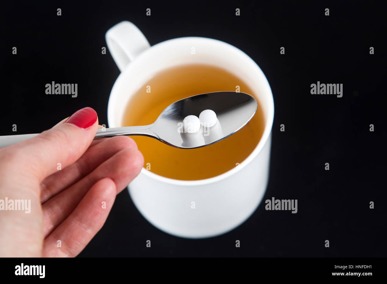 Hand holding a spoon with sweetener with a cup of tea in the background Stock Photo