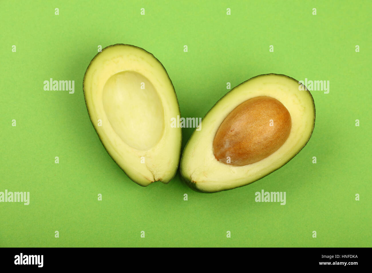 Two halves of one fresh ripe cut avocado with pit stone on green paper background, detail, close up, elevated top view Stock Photo