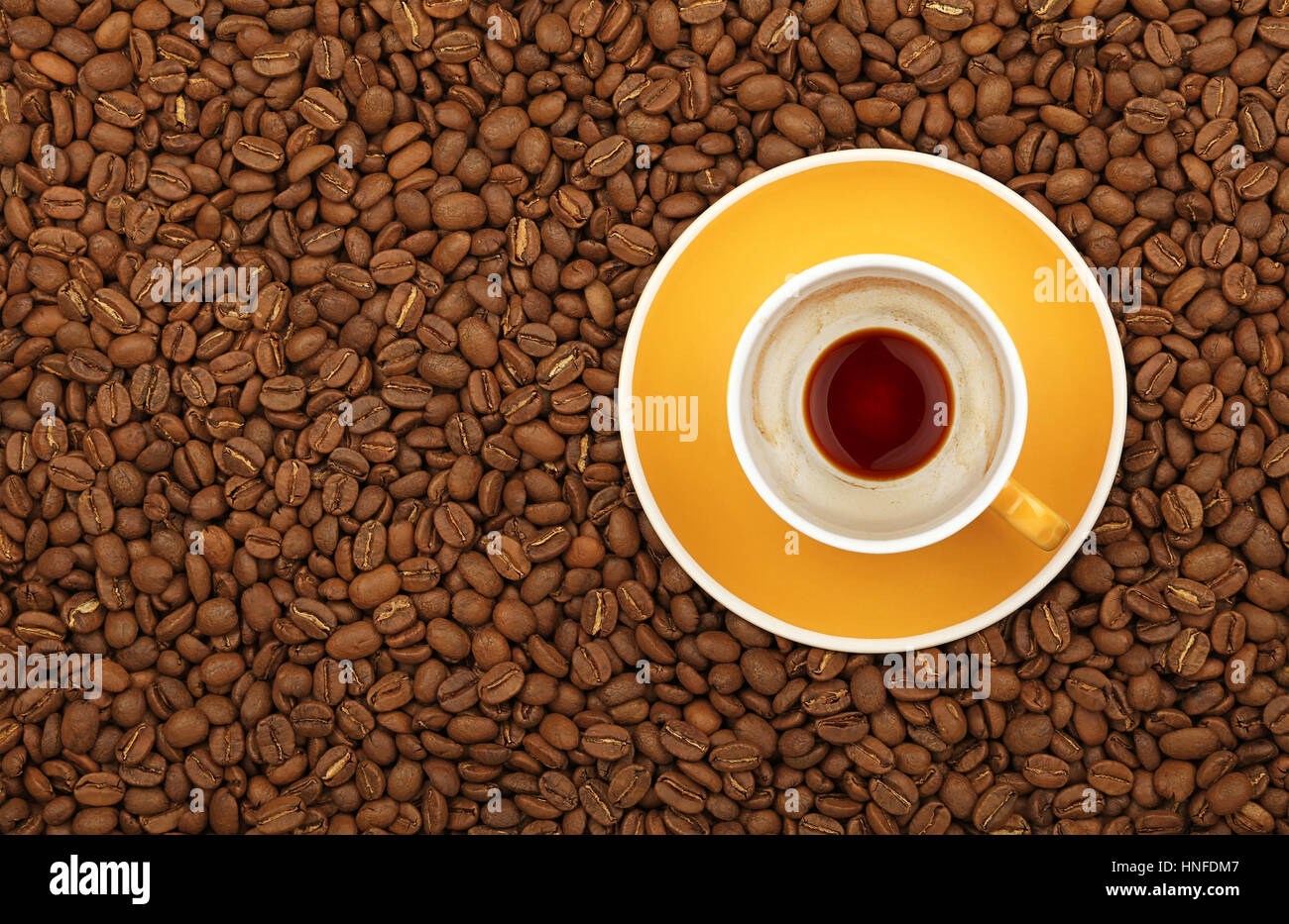 Empty black coffee yellow cup with saucer on background of roasted