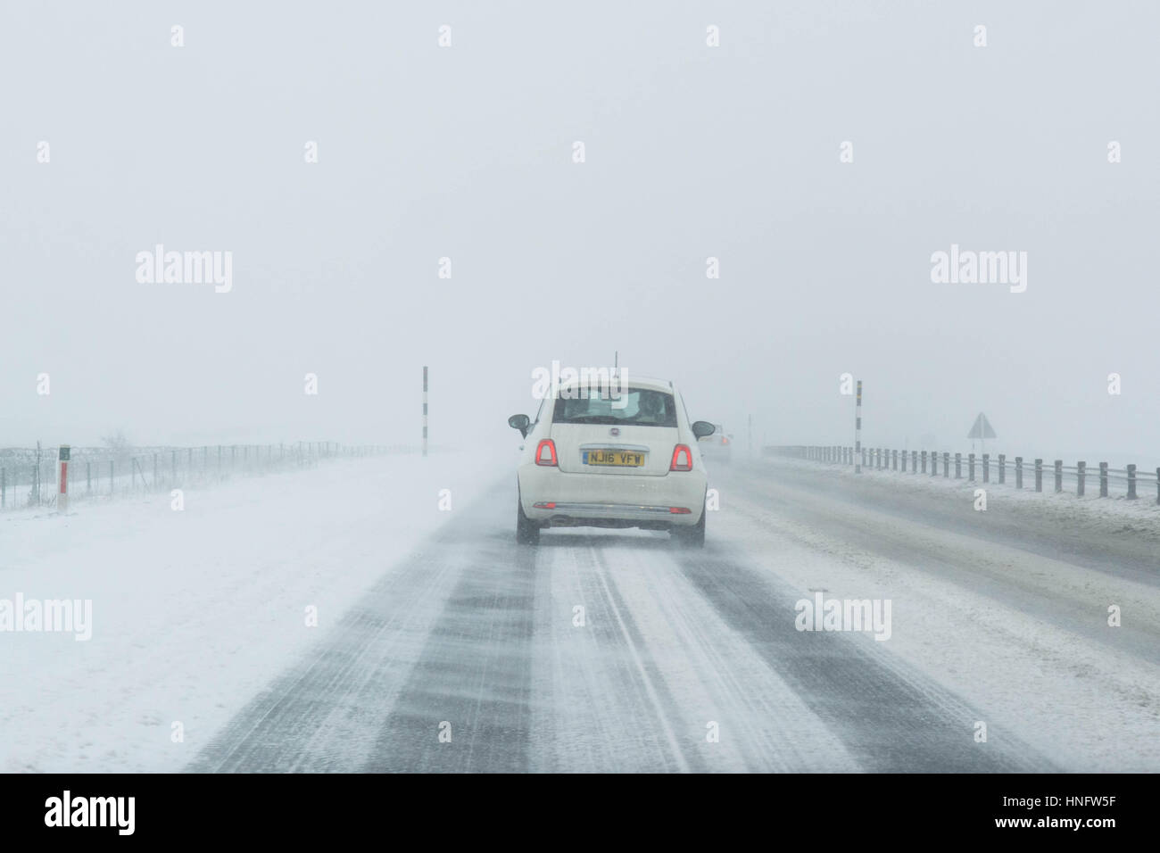 white car driving on A66 road in Northern England in winter in drifting snow Stock Photo