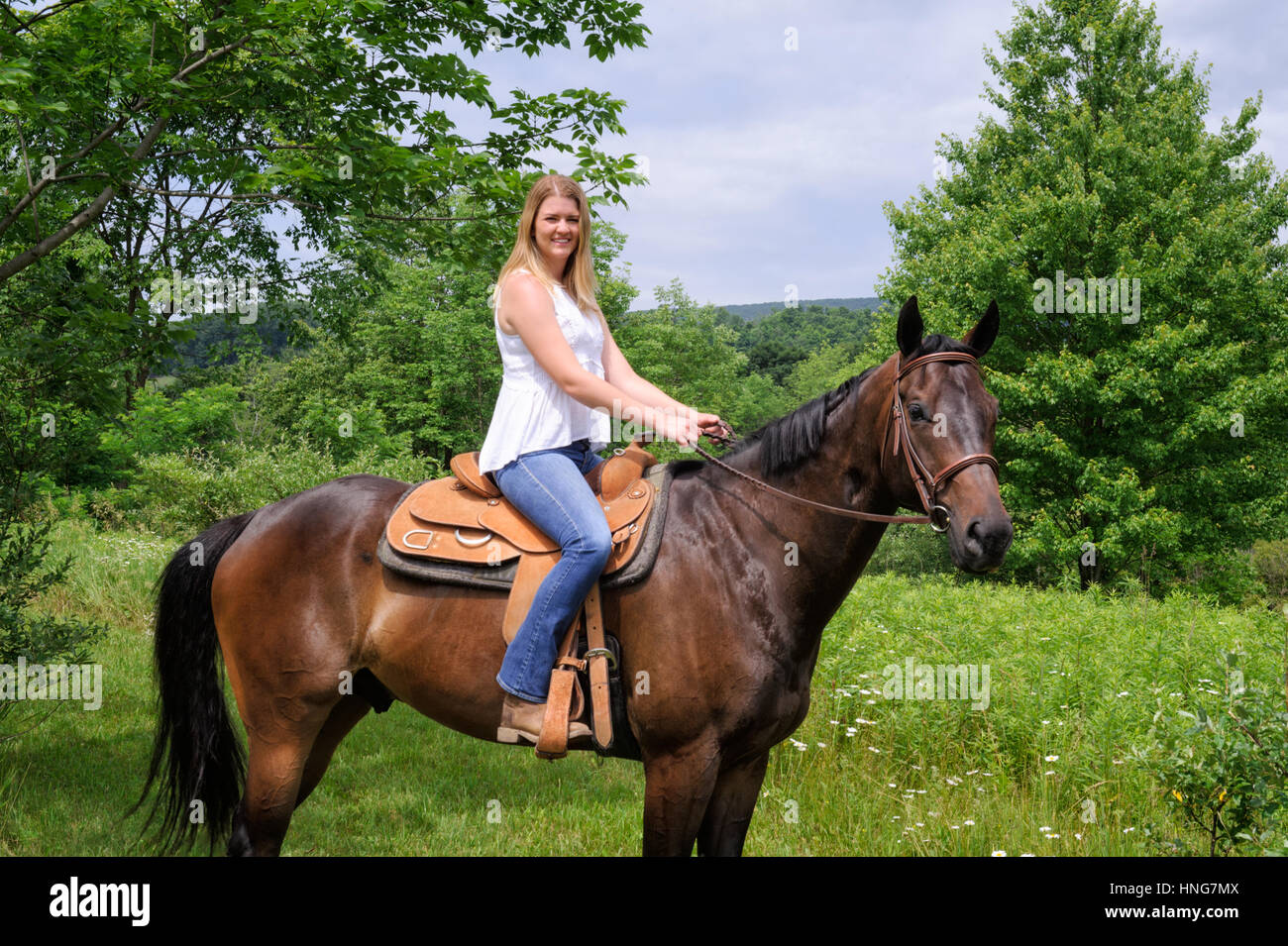 Girl, on a brown western saddle, horseback riding, surrounded by green foliage on a summer trail