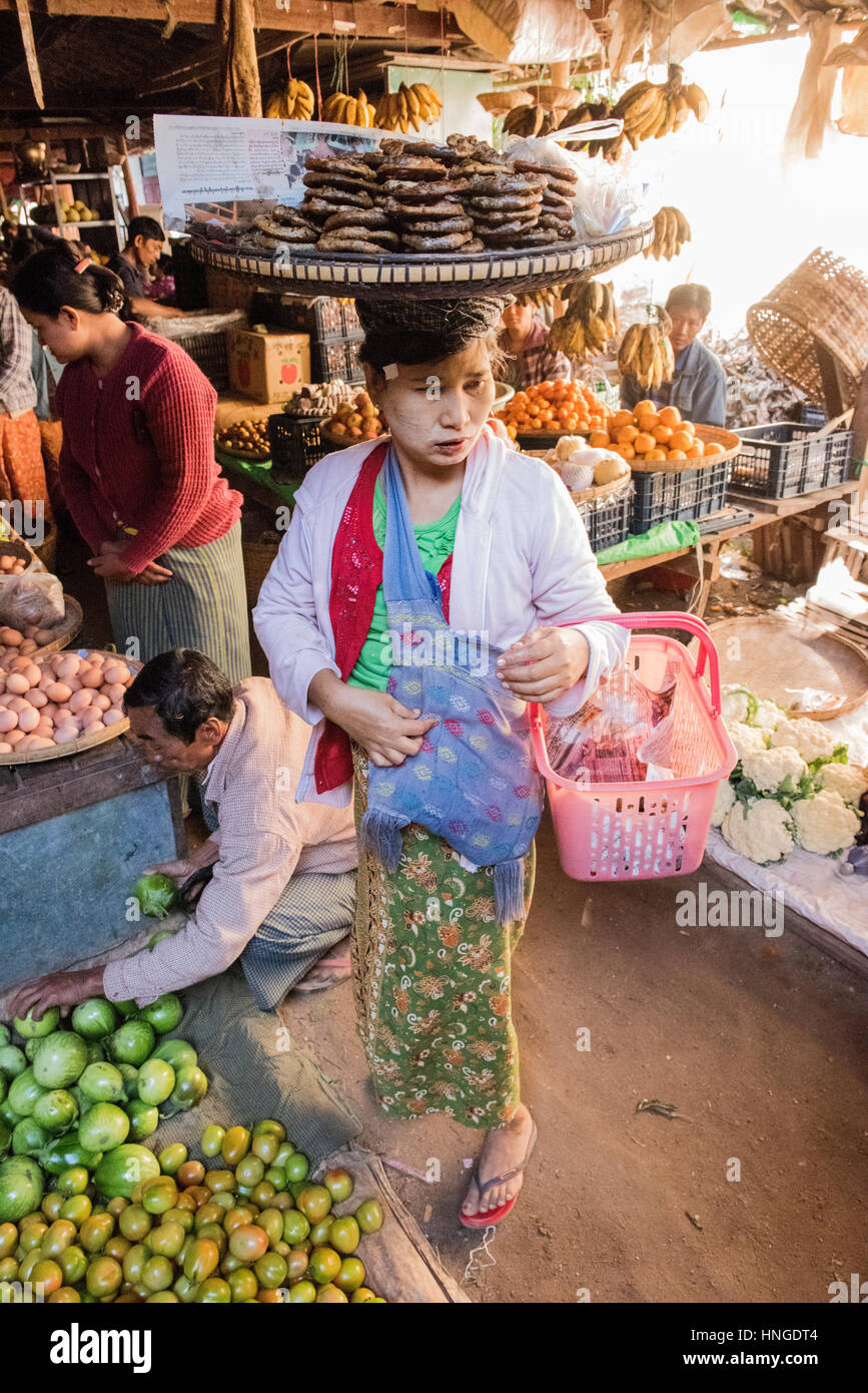 female market trader balancing produce on her head in local dress working in Stock Photo