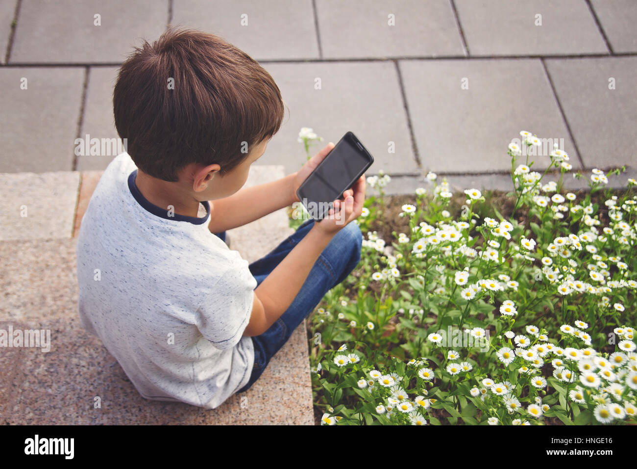 Little boy with smartphone sitting on stairs in city park. Technology, education and lifestyle concept Stock Photo