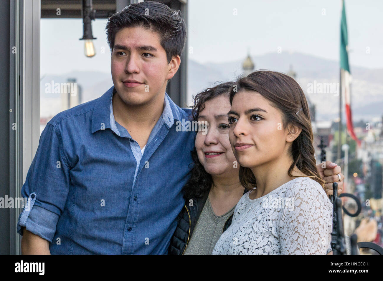 family portrait on rooftop dining terrace of Holiday Inn includes proud Mexican mother with handsome adult son & stylish pretty daughter Stock Photo