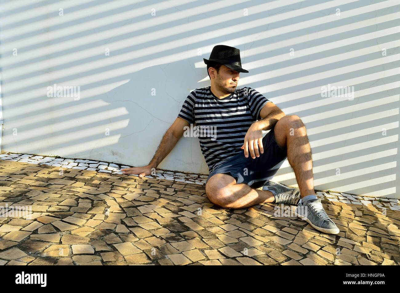 Man sitting on the ground leaning against a wall Stock Photo