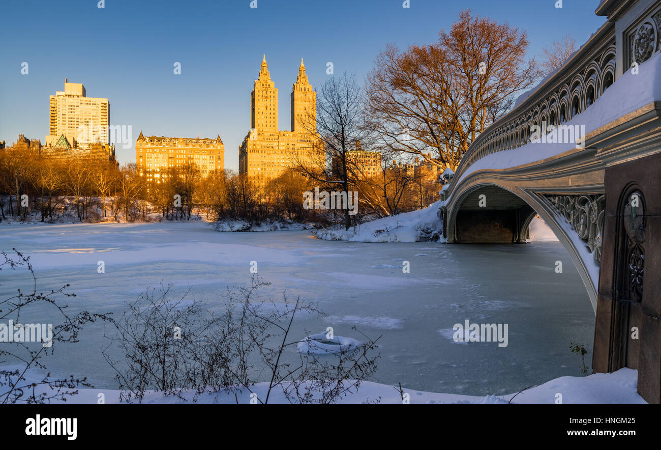 Central Park winter sunrise on the frozen Lake with the Bow Bridge and Upper West Side buildings. Wintertime in Manhattan, New York City Stock Photo