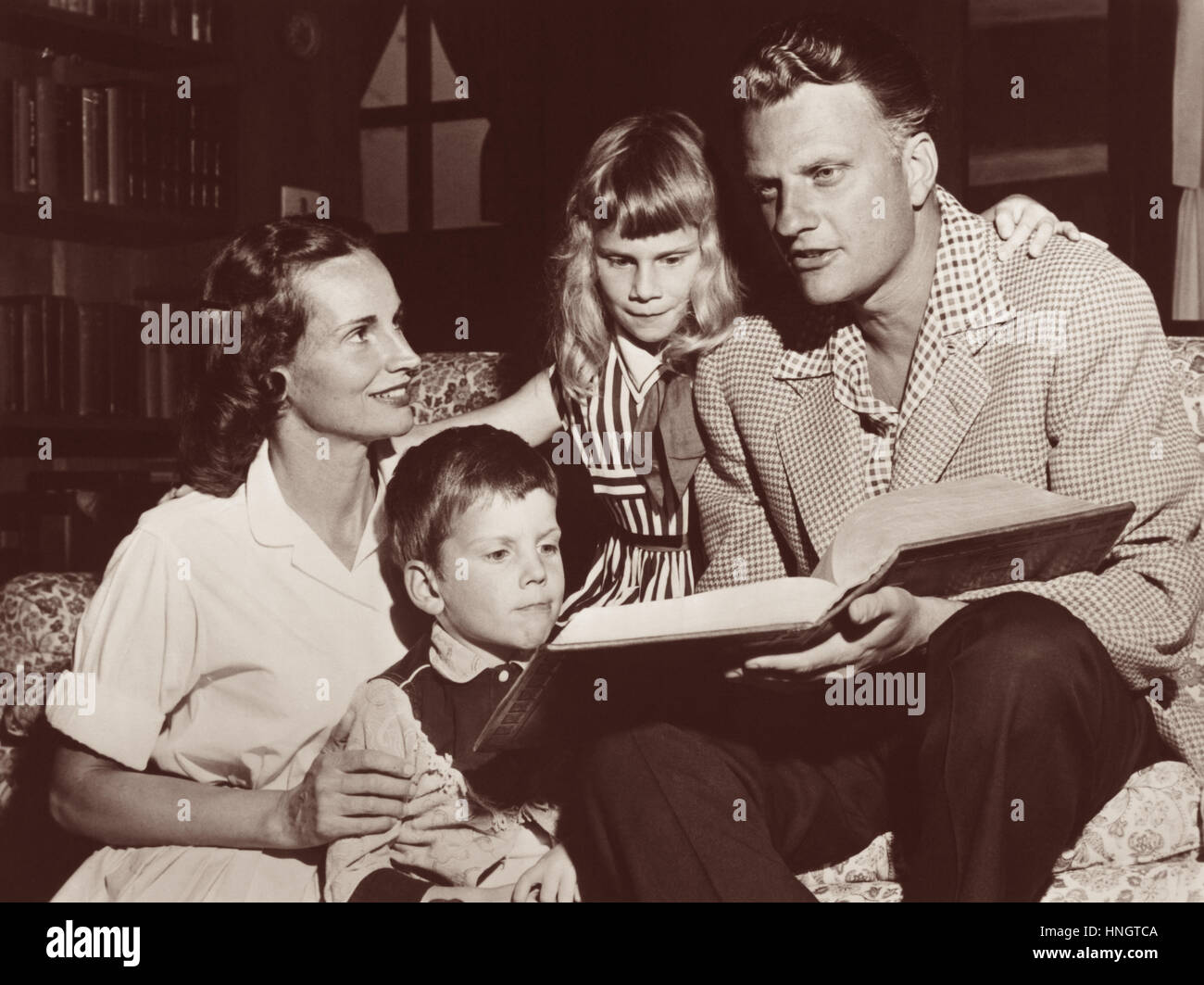 Evangelist Billy Graham reading from a family Bible with wife Ruth and their children in the Graham's Montreat, North Carolina home in 1957. Stock Photo