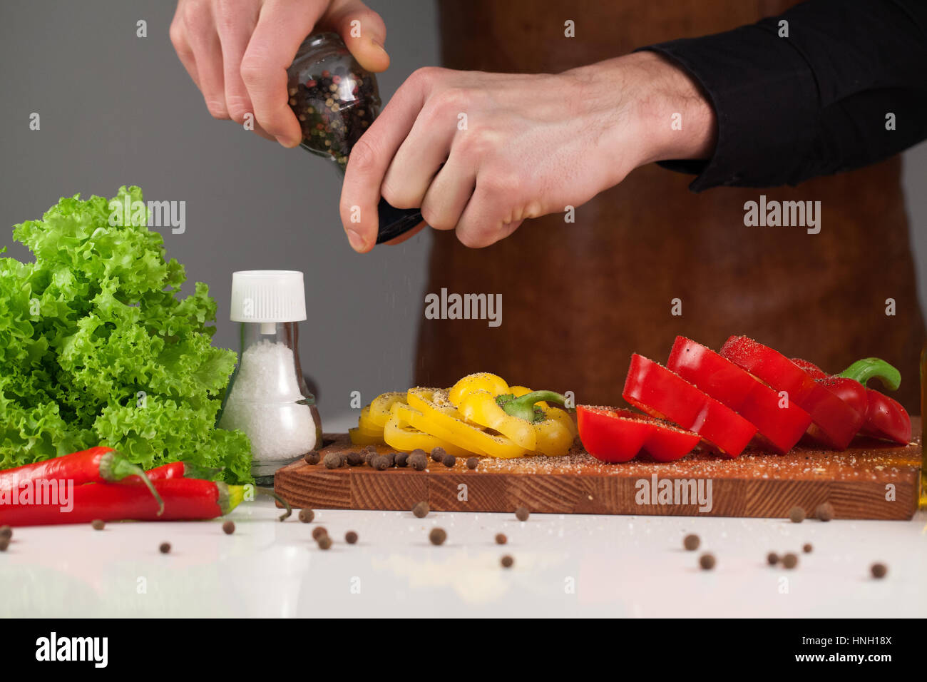 Man using pepper-mill while making a salad. Set of coloured vegetables on a wooden cutting board Stock Photo