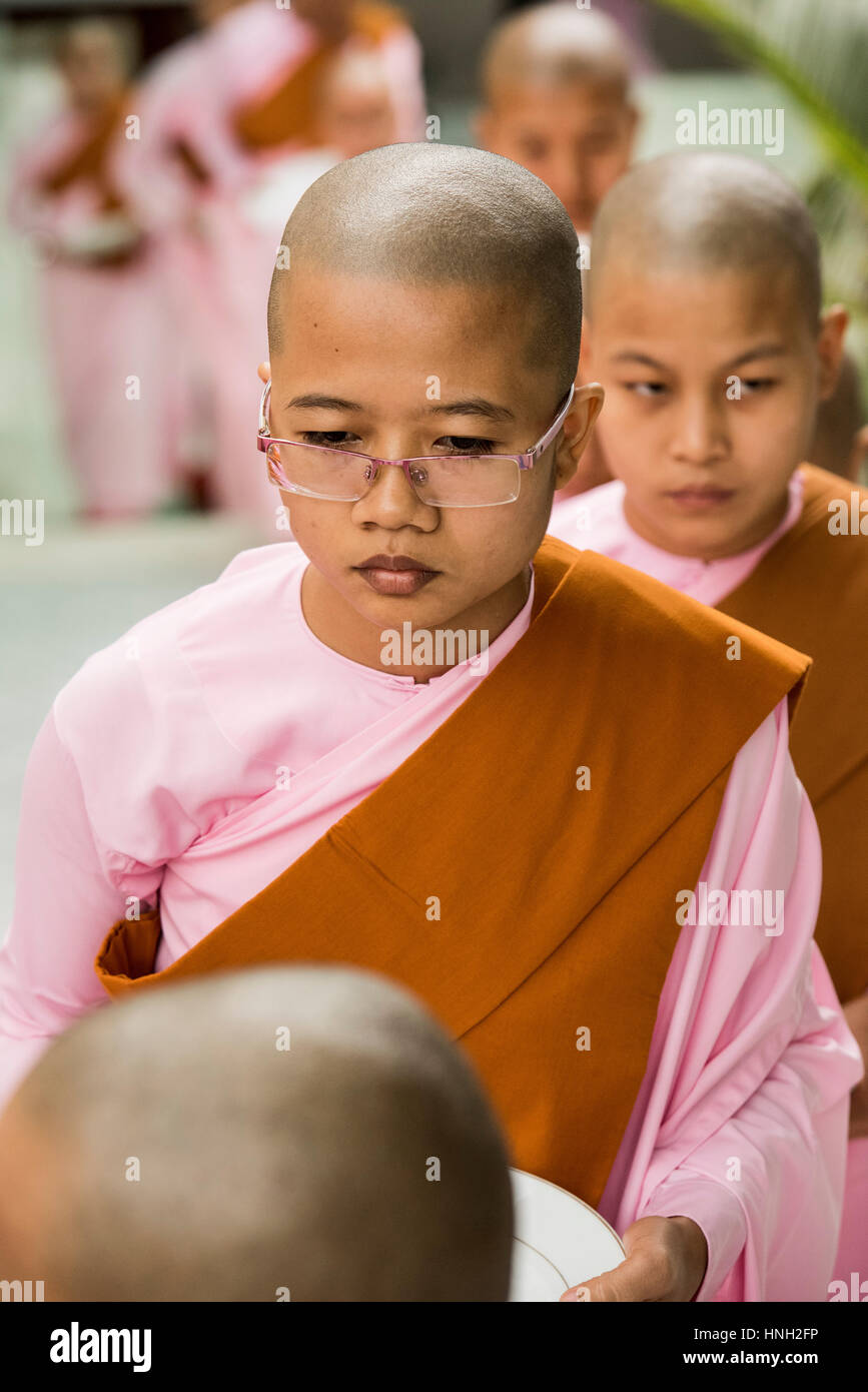Buddhist nuns in their distinctive pink robes and shaved heads lining up to have lunch in Yangon Stock Photo