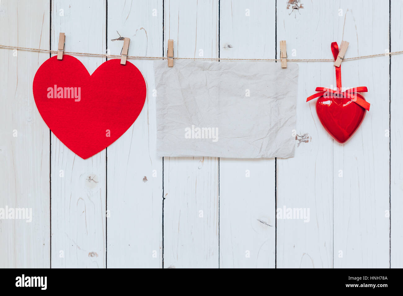Red heart and old paper blank hanging at clothesline on wood white background with space. Valentine Day. Stock Photo