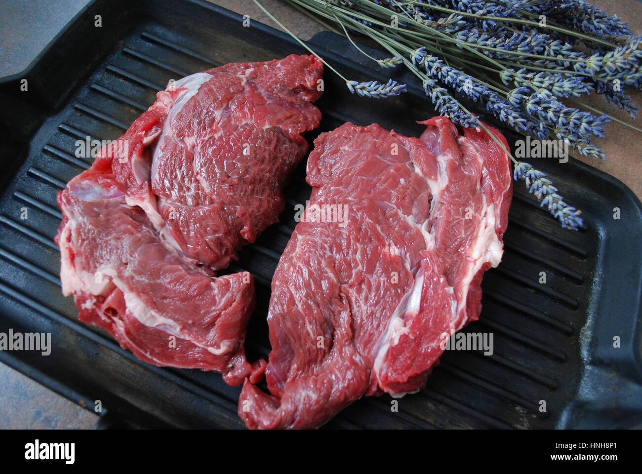 Fresh beef steak on a grill. Lavender branch on the background. Stock Photo